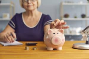 Elderly woman woman sitting with notes and putting coins to piggybank for saving money to pay for nursing home care