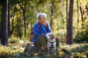 A senior woman with dog on a walk outdoors in forest, resting. Emotional Support Animal