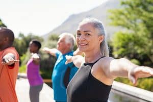 Reducing fall risk. Portrait of happy senior woman practicing yoga outdoor with fitness class. Beautiful mature woman stretching her arms and looking at camera. Portrait of smiling ladywith outstretched arms at park.