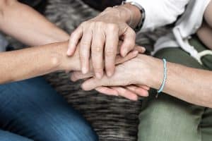 close up of senior citizen and younger adult holding hands in support