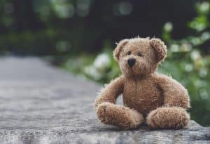 Teddy bear with sad face sitting on footpath blurry background