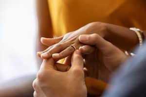 Close up of man putting engagement ring on his girlfriend hand. Community Property.