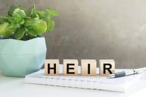 HEIR word made with building blocks on the table next to a flower in a pot and a notebook with a pen. Legal terms in estate planning.