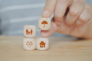 hand holding umbrella icon on wooden cube block over family, heart and house symbol for health, property ,life, family, group insurance