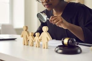 Judge With Magnifying Glass Looking At Little Family Figures Guardianship