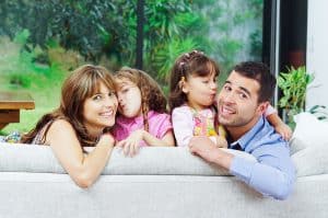 Family of four looking over the back of a couch smiling