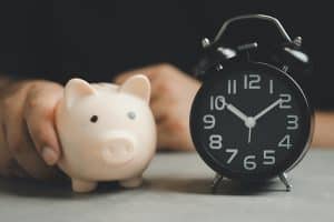 Hand holding a piggy bank and alarm clock. The concept for saving time. Saving time investment budget wealth business retirement, financial, money, banking concept. Beneficiary waiting for money.