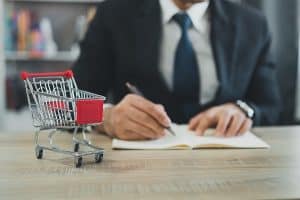 Business man wearing suit and calculates the budget. Shopping cart a on table with note book. Budget of poor low income family. Rising food and grocery store prices and expensive daily consumer goods.