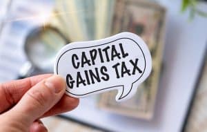 Capital Gains Tax text in cartoon caption bubble, faded currency in background