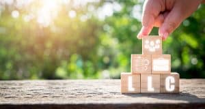 Wooden blocks spelling out LLC with other blocks displaying business concepts stacked in a pyramid outside on a sunny day