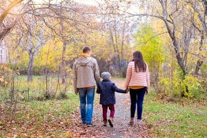 Family of three walks in the autumn park holding hands on the road representing choosing guardian and trustee