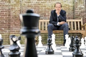 man on park bench in front of life size chess game, planning his next move