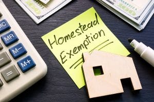 Homestead Exemption written on a sticky note with a wooden home cut out on top next to a calculator