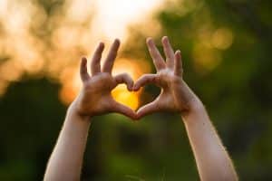 Heart shape hand of kid's body language for children's love, kindness, love concept. Heart Hand on nature sunset bokeh background demonstrating love languages and estate planning.