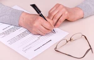 hands of a woman filling out a MPOA form with a set of reading glasses near her on the table
