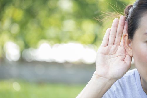 Woman holds her hand near ear with symptom of hearing loss