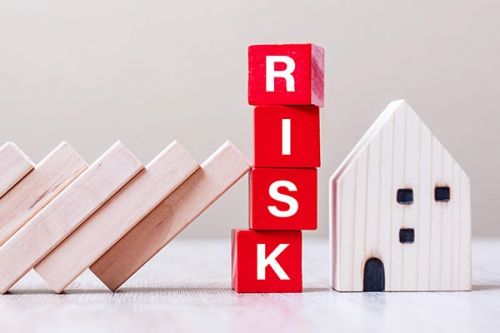 RISK in red wooden blocks keeping other blocks from falling on a wooden house