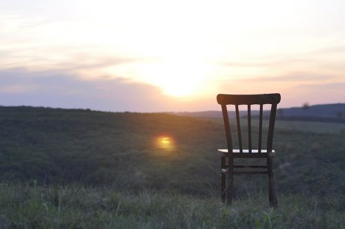 An old antique chair stands on the grass. At sunset. Summer. The concept of loneliness.