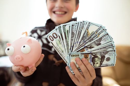 Happy young child holding a lot of cash and a piggy bank