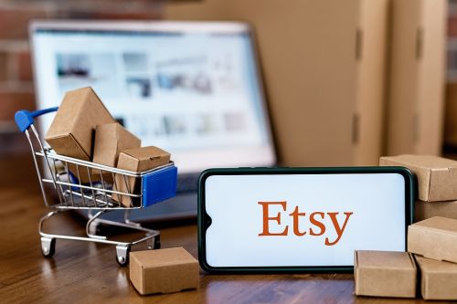 Smartphone with Etsy store logo on the screen, shopping cart and laptop.