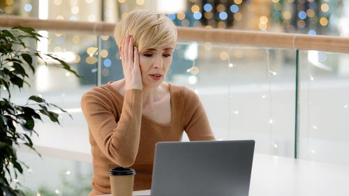 woman in front of open laptop with coffee next to her, hand on face in crisis
