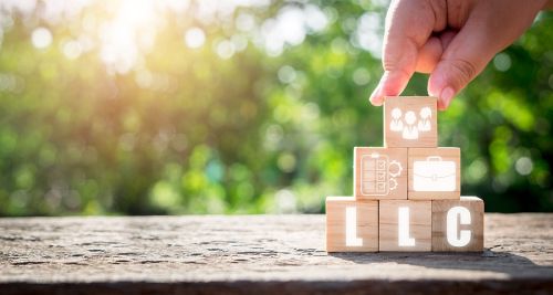 Wooden blocks spelling out LLC with other blocks displaying business concepts stacked in a pyramid outside on a sunny day