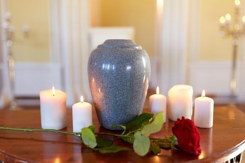 funeral and mourning concept - red rose and cremation urn with burning candles on table in church