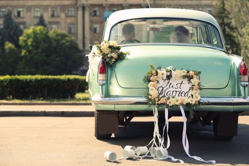 Wedding couple in car decorated with plate JUST MARRIED and cans