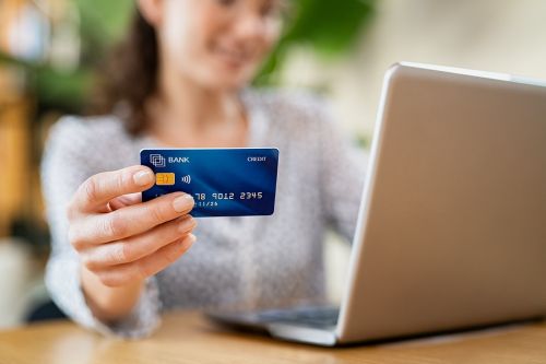 Close up hand of young woman holding credit card while making online payment. Woman hands holding a debit card and using laptop to do shopping online. Smiling girl with bank card paying bills online.