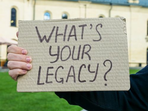 Persn holding a sign written on cardboard WHAT'S YOUR LEGACY?