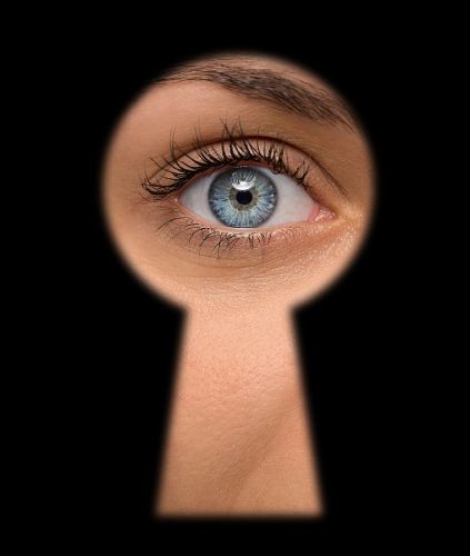 Close up of shocked female eye looking through a keyhole who is nosey neighbor
