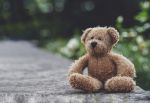 Teddy bear with sad face sitting on footpath blurry background, Loneliness.