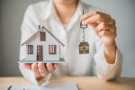 person holdnig a model of a house in one hand and a set of keys with a house keychain in the other