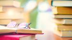 Eyeglasses on an open book, surrounded by stacks of books