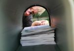 A man peering into a full mailbox trying to stop mail of a deceased person