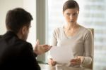 business woman with a skeptical expression is looking at a document that is being explained by a man sitting across from her