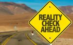 Yellow road sign that reads Reality Check Ahead on a desert canyon road