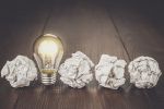4 crumpled balls of paper and one lit light bulb in a row